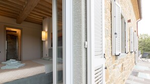 A hotel room with a bed, a window with shutters, and a view of the outside.