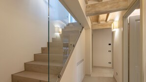 A modern staircase with glass railings and wooden steps, leading to a hallway with a door and a light switch on the wall.