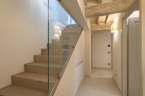 A modern staircase with glass railings and wooden steps, leading to a hallway with a door and a light switch on the wall. - Wonderful private villa for 8 people with private pool, WIFI, A/C, veranda and panoramic view (Cortona)
