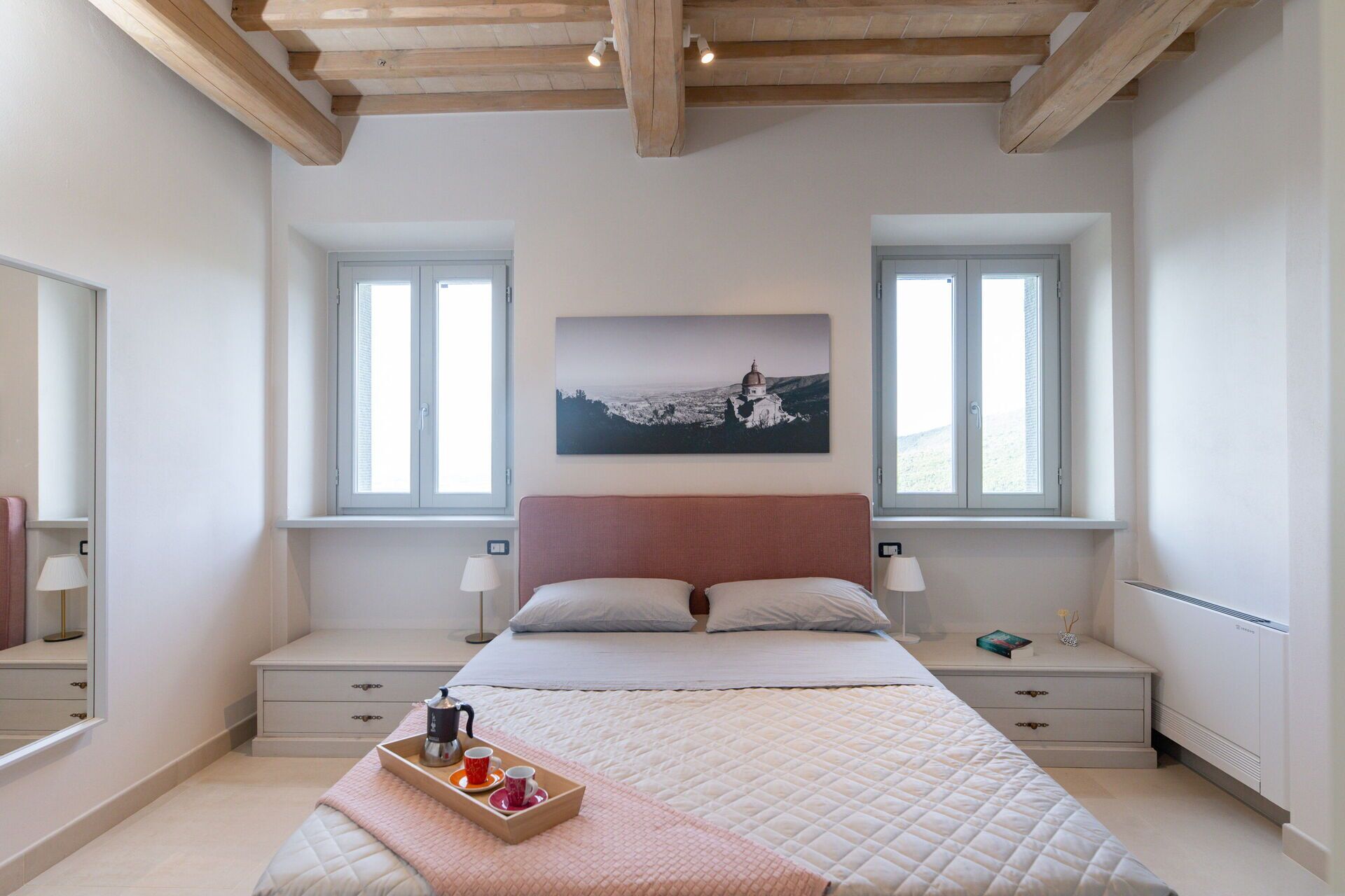 Un dormitorio con cama, mesitas de noche, un cuadro en la pared y una ventana.
