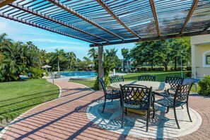 Eine überdachte Terrasse mit Pool, Sitzgelegenheiten im Freien und üppiger Bepflanzung.