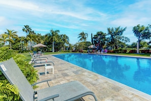Ein Pool mit Liegestühlen und Sonnenschirmen, umgeben von Palmen und Grünpflanzen.
