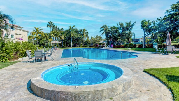 Una piscina con hidromasaje, rodeada de sillas de descanso y palmeras.
