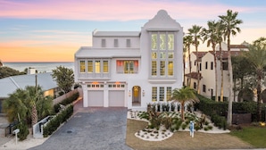 A large, white, two-story house with a prominent tower, a driveway, and a well-maintained garden with palm trees. - 'Domus Pacis' | Two Pools, Beach Front,  Next to Seaside 30A (Seagrove Beach)