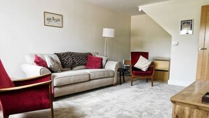 Una sala de estar con un sofá, un sillón rojo, una silla de madera, una mesita y una lámpara.