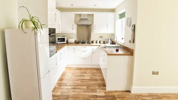 Una cocina moderna con gabinetes blancos, encimera de madera y horno empotrado.
