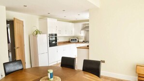 Cocina compacta con armarios blancos, microondas y estufa. Hay una mesa de comedor con cuatro sillas y una planta pequeña en la encimera.