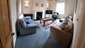 A spacious living room with a fireplace, a blue sofa, a beige sofa, and a coffee table. - Stunning 3BD Victorian House in Bramhall Village (Bramhall)