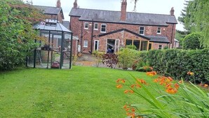 A brick house with a glass conservatory, a well-maintained lawn, and orange flowers in the foreground. - Stunning 3BD Victorian House in Bramhall Village (Bramhall)