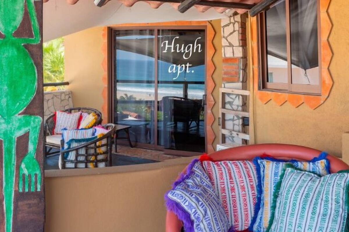 Un ambiente accogliente con una panca in legno, un'area salotto con cuscini e una finestra con la scritta "Hugh apt".