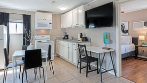 A compact kitchen with white cabinets, a microwave, a stove, and a coffee maker. There is a dining table with two chairs. A flat-screen TV is mounted on the wall above the counter. - The Palm Flats 16! Zoo! Museums! Medical Center! (Houston)