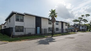 A two-story apartment building with a black metal fence, a palm tree, and a blue door. - The Palm Flats 16! Zoo! Museums! Medical Center! (Houston)