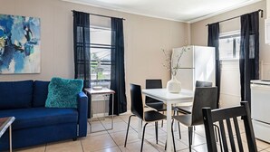 A compact living space with a blue sofa, a dining table with chairs, a white refrigerator, and a large abstract painting on the wall. - The Palm Flats 16! Zoo! Museums! Medical Center! (Houston)
