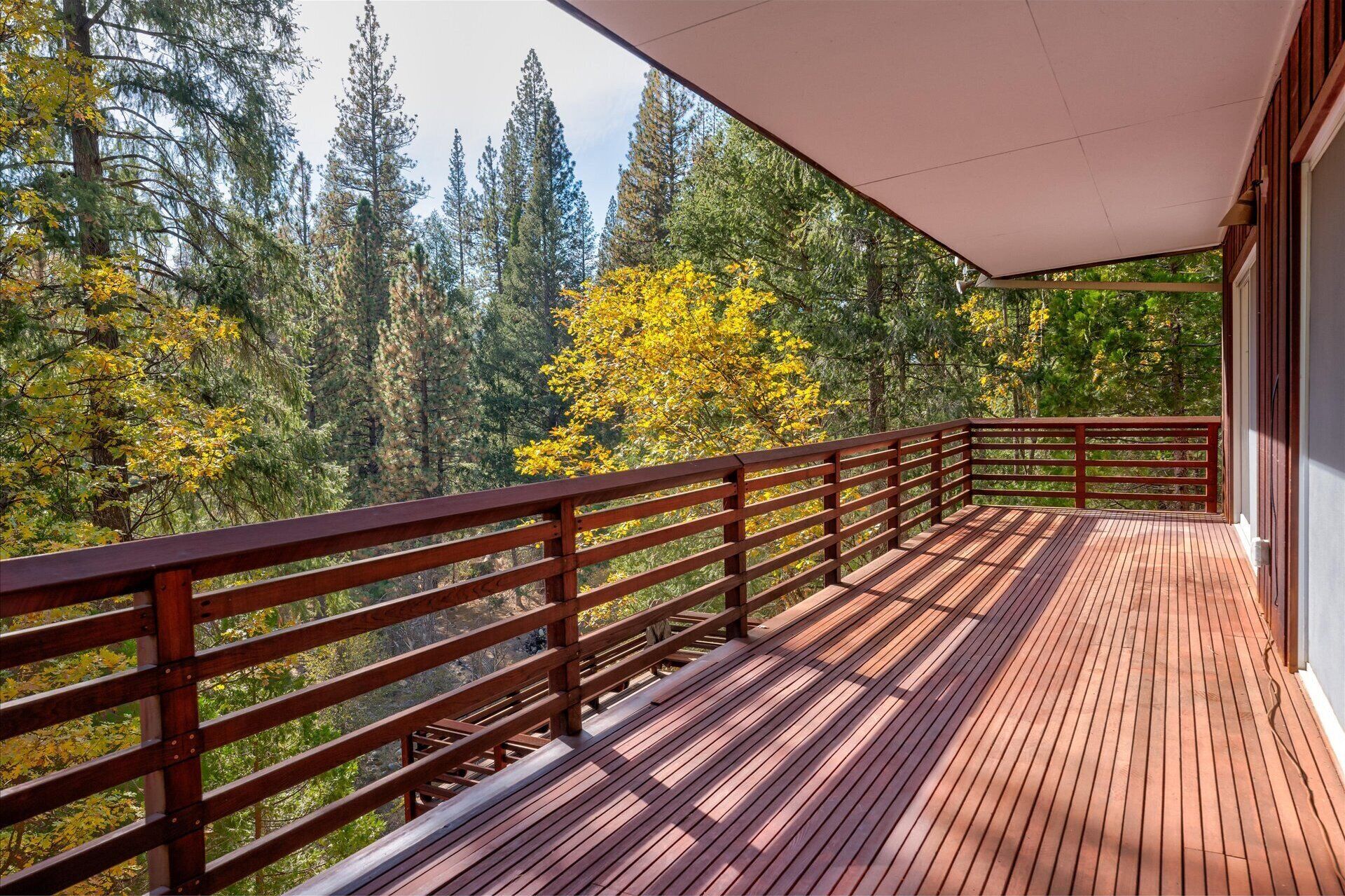 A wooden deck with a railing overlooking a forested area with autumn foliage.