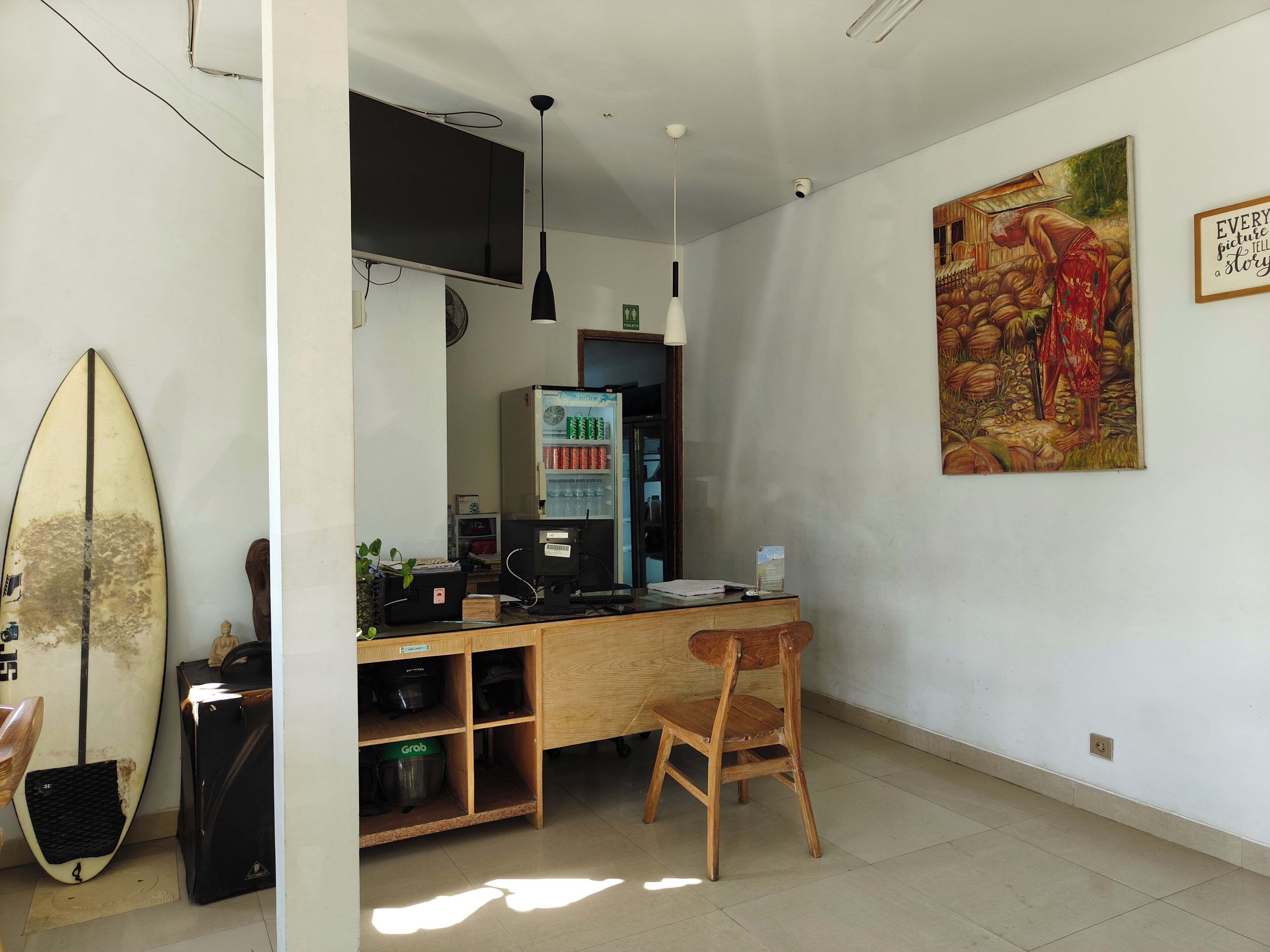 Una habitación con una tabla de surf, una máquina expendedora, un escritorio de madera y una silla.