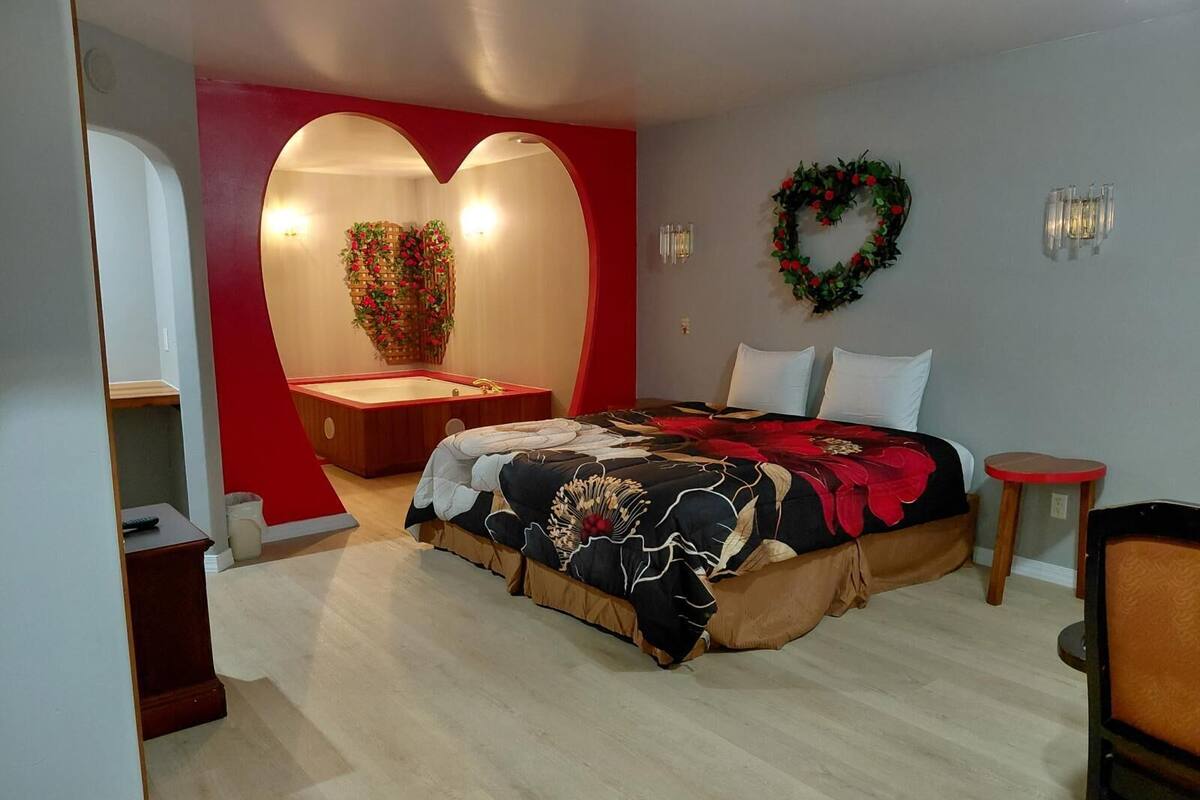 A bedroom with a bed, a heart-shaped wall, a bathtub, and a wall-mounted wreath.