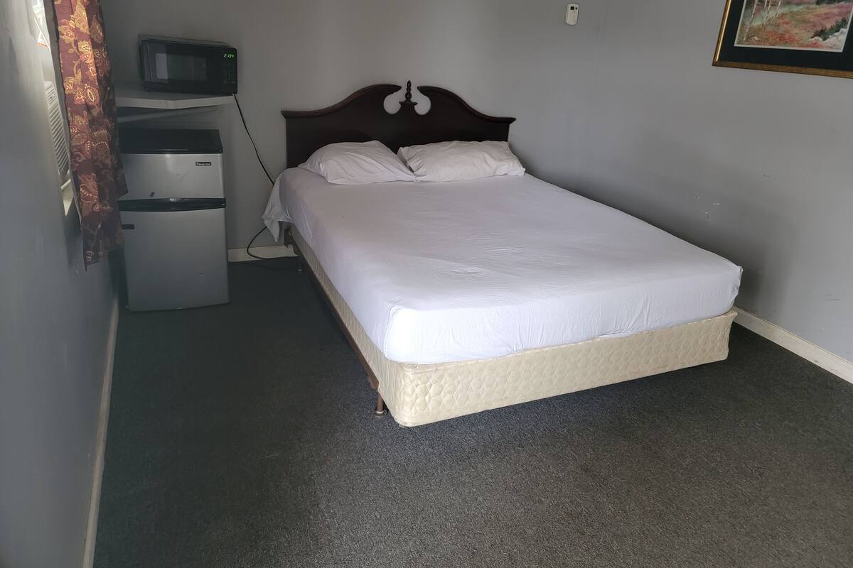 A bedroom with a bed, a small refrigerator, a microwave, and a framed picture on the wall.