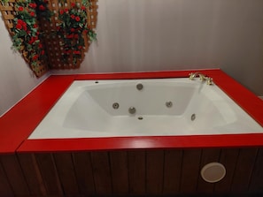 A rectangular bathtub with a red border, a wooden panel design, and a built-in drainage system. - Grand Howell Inn (Howell)
