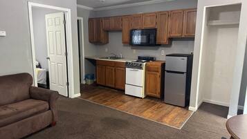 A compact kitchen with wooden cabinets, a microwave, a stove, and a refrigerator.