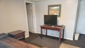 A living room with a brown leather sofa, a wooden coffee table, a TV on a stand, and a framed picture on the wall. - Grand Howell Inn (Howell)
