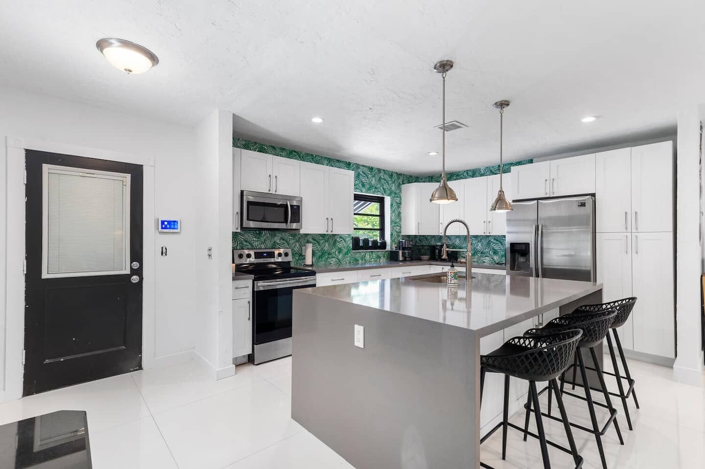 A modern kitchen with a central island, stainless steel appliances, and a black-framed window.