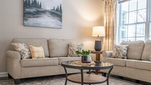 Un salon avec un canapé beige, une table basse ronde et un tableau accroché au mur.
