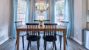 Un coin repas avec une table en bois et des chaises noires, des rideaux bleu clair et un lustre.