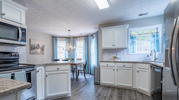 Une cuisine avec des armoires blanches, un four à micro-ondes, une cuisinière et un lave-vaisselle. On y trouve une table à manger avec des chaises et un lustre.