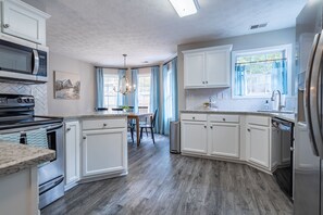 A kitchen with white cabinets, a granite countertop, a stainless steel refrigerator, and a dishwasher. - Weekly Rates: Serene 3BR Home on Expansive Grounds (Kingston)