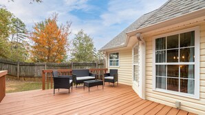 Une terrasse avec des meubles d’extérieur, une clôture en bois et une maison dotée de grandes fenêtres.