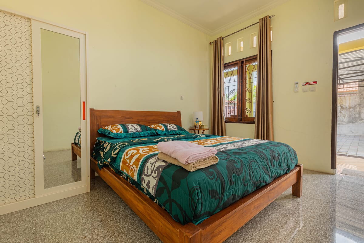 A bedroom with a wooden bed, patterned bedding, a bedside table with a lamp, and a window with curtains.