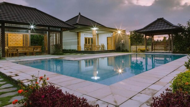A swimming pool with a tiled deck, a covered seating area, and a gazebo. - Bait Nahwa  (Narmada)