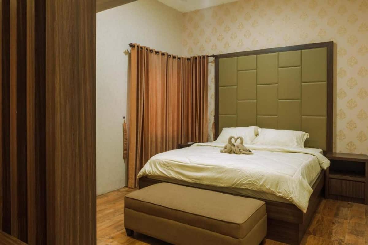 A hotel room with a large bed, a wooden nightstand, a brown bench, and a patterned wallpaper.