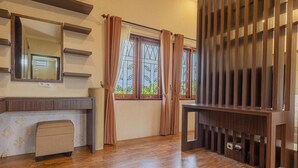 A room with a wooden floor, a small beige sofa, a wooden console table, a mirror, and a window with decorative metal bars. - Bait Nahwa  (Narmada)