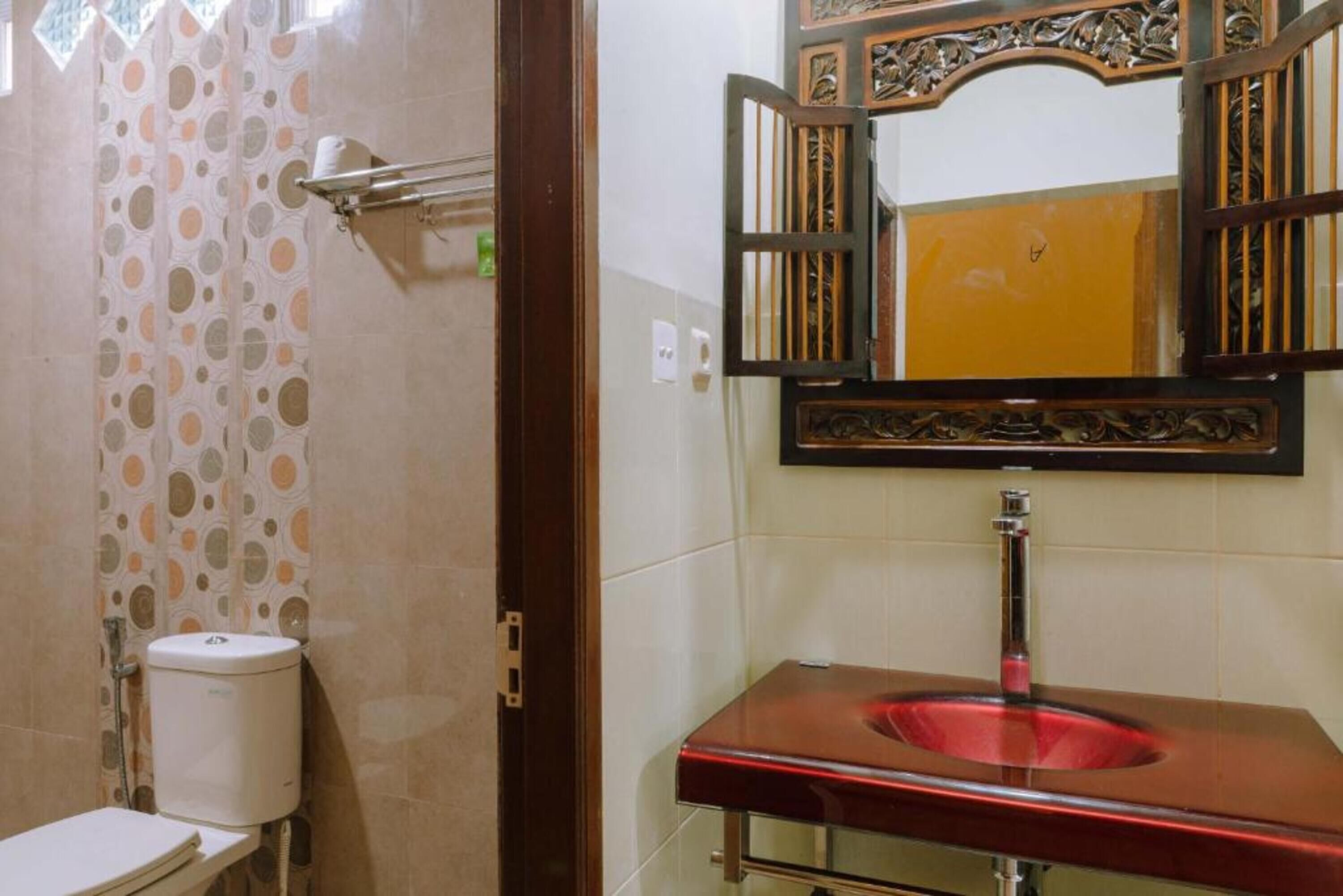 A bathroom with a toilet, a sink with a red basin, and a mirror with an ornate frame.