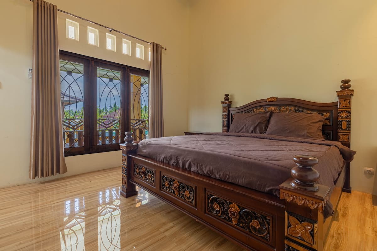 A bedroom with a large bed, a window with curtains, and a wooden floor.