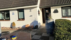 Une maison à deux étages, avec un toit recouvert de tuiles, une petite fenêtre et une porte ornée d’une enseigne décorative.