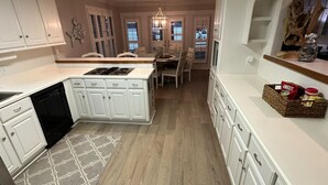 A modern kitchen with white cabinetry, a central island, and a dining area with a chandelier.
