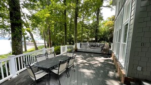 A covered deck with a table and chairs, surrounded by white railings and trees.