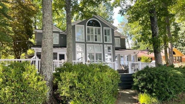 A two-story house with a covered porch, surrounded by mature trees and well-maintained bushes.