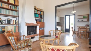 A living room with a fireplace, bookshelves, wicker furniture, and a kitchen area visible through an open door. - 3 bedroom lovely home in Santa Croce Camerina (Santa Croce Camerina)