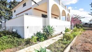 A white building with a balcony and arched windows, surrounded by greenery and a stone pathway. - 3 bedroom lovely home in Santa Croce Camerina (Santa Croce Camerina)