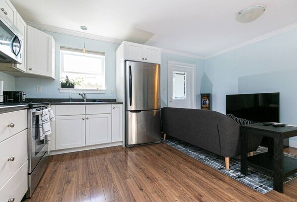 A compact kitchen with white cabinets, a stainless steel refrigerator, a built-in oven, and a black dining table.