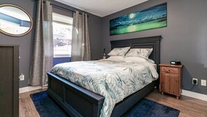Une chambre à coucher avec un grand lit, une table de chevet, un tableau et une fenêtre avec des rideaux.