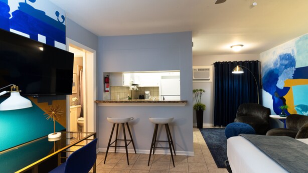 A modern living room with a flat-screen TV, a glass coffee table, two bar stools, a sofa, and a ceiling fan. - Studio @ Montrose 01! Downtown, Medical Center, Stadium (Houston)
