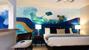 A hotel room with a bed, two bedside tables with lamps, a chair, and a wall mural. - Studio @ Montrose 01! Downtown, Medical Center, Stadium (Houston)