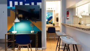 A modern kitchen with a flat-screen TV, a bar area with stools, and a dining table with chairs. - Studio @ Montrose 01! Downtown, Medical Center, Stadium (Houston)