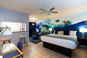 A modern hotel room with a large bed, a desk with a chair, a ceiling fan, and a mural on the wall. - Studio @ Montrose 01! Downtown, Medical Center, Stadium (Houston)