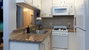 A kitchen with white cabinets, a granite countertop, a gas stove, a microwave, and a refrigerator. - Studio @ Montrose 01! Downtown, Medical Center, Stadium (Houston)