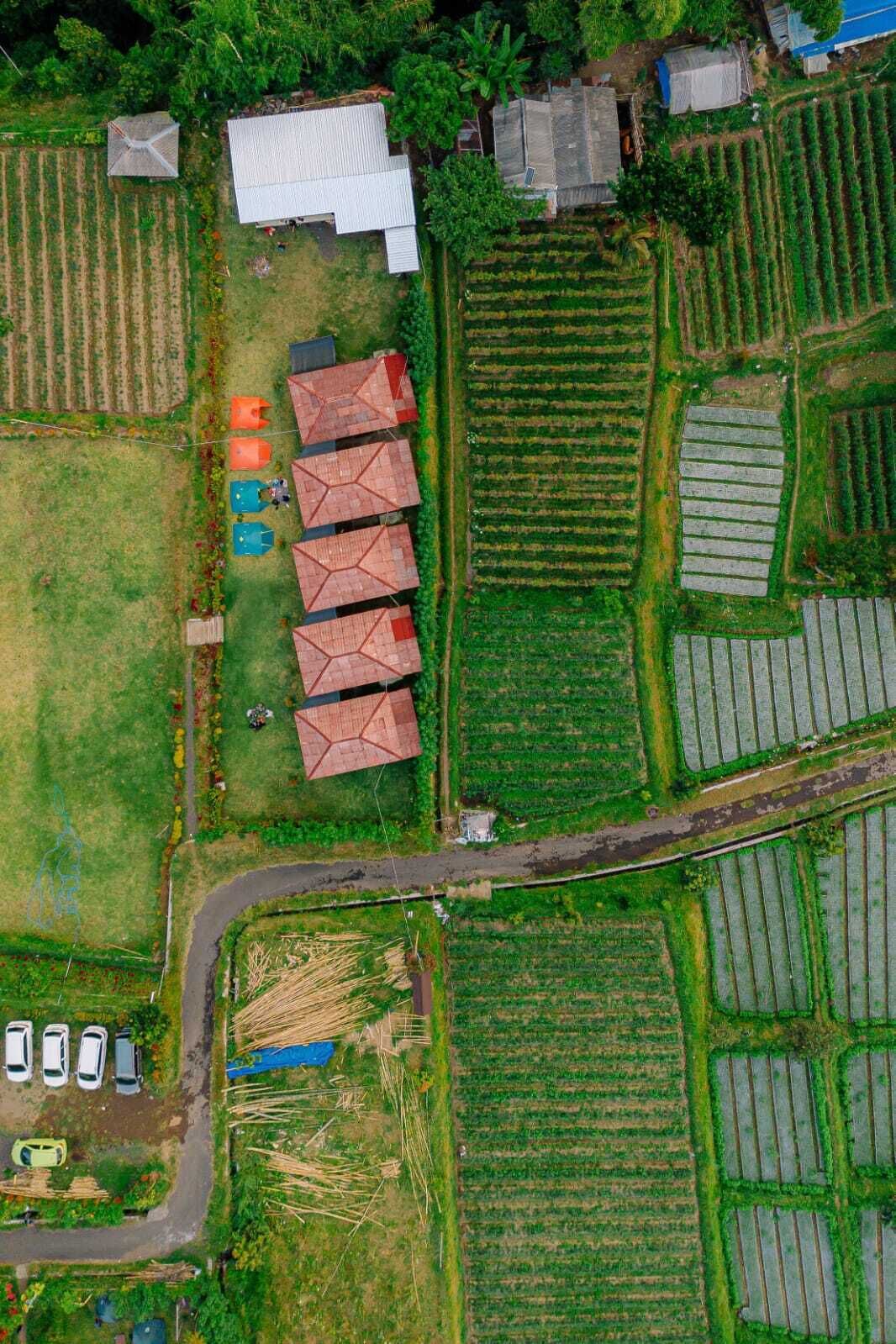 Luchtbeeld van een landelijk gebied met verschillende velden, enkele gebouwen en een weg.